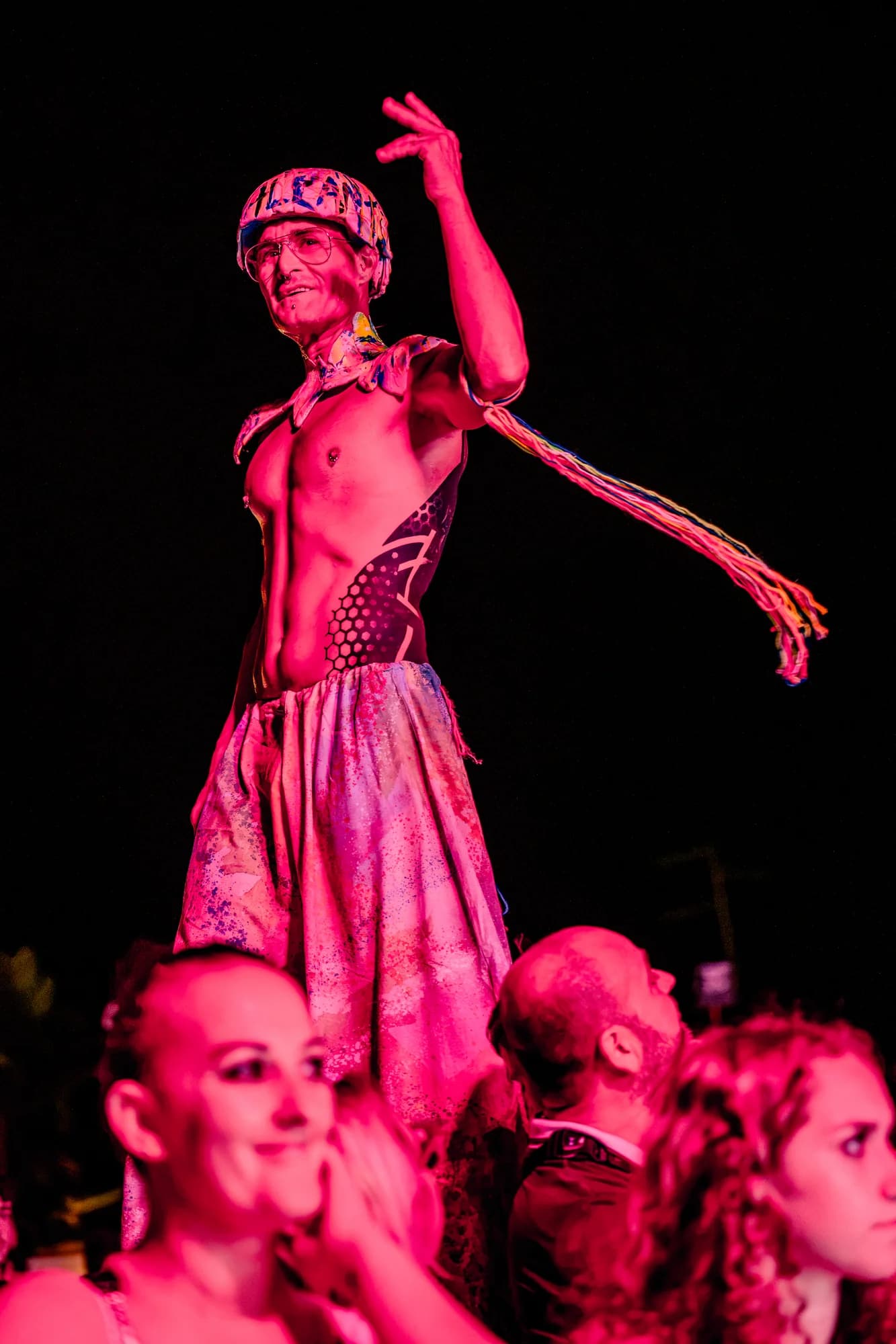 Performer in alto tra il pubblico sotto le luci rosa